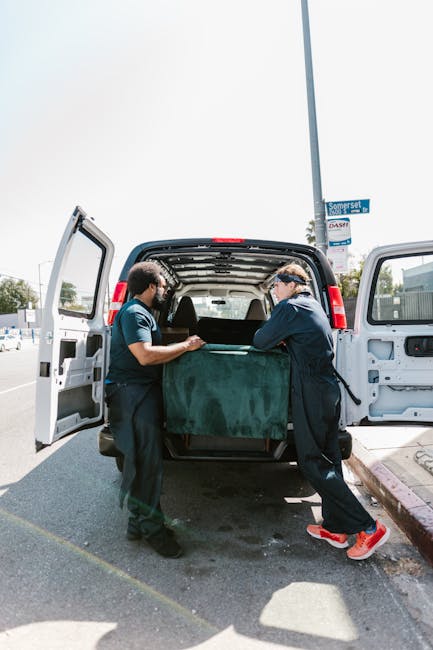 Two movers from Man and Van Harringay are engaged in the loading process of a household relocation, carefully carrying a large piece of furniture covered with a green protective blanket into the open